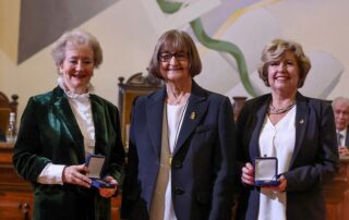 La profesora María Teresa Infante Caffi (a la izquierda) y la profesora Mónica Rubio López (a la derecha) reciben la Medalla Rector Juvenal Hernández Jaque 2024 de la rectora de la Universidad de Chile, la profesora Rosa Devés Alessandri (al centro), el 30 de abril de 2025 en el Salón de Honor de la Casa Central de la Universidad de Chile. Crédito fotográfico: redes sociales del Senado de Chile.